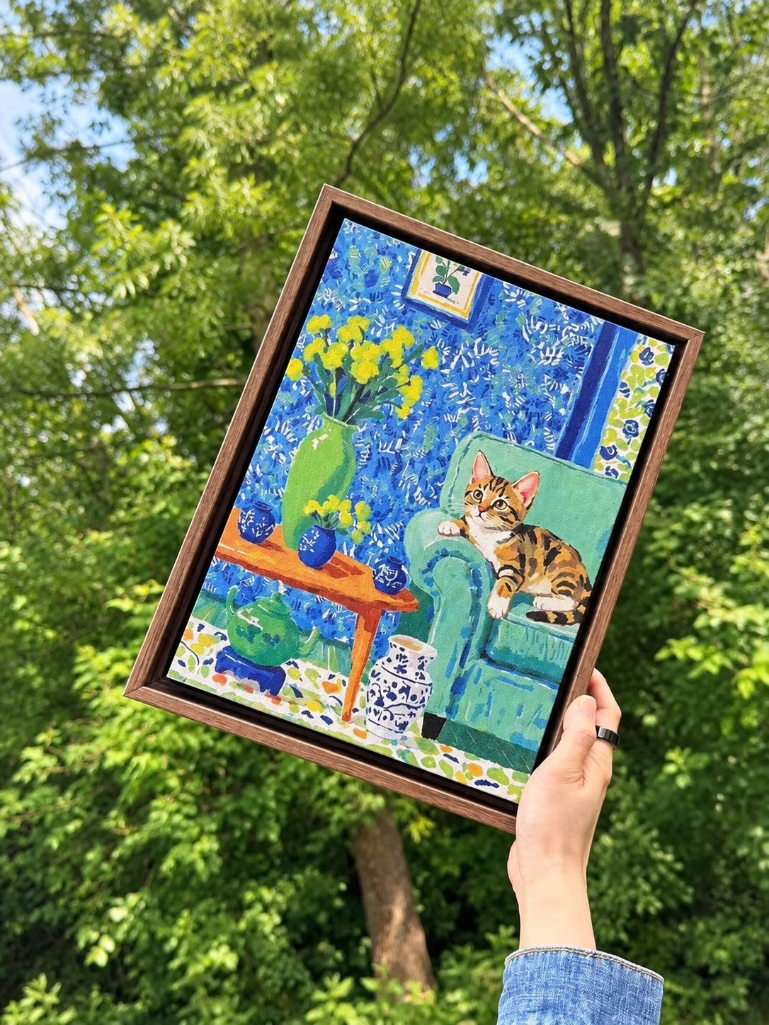 Framed custom cat portrait on canvas featuring a tabby cat lounging on a green chair in a colorful interior scene.