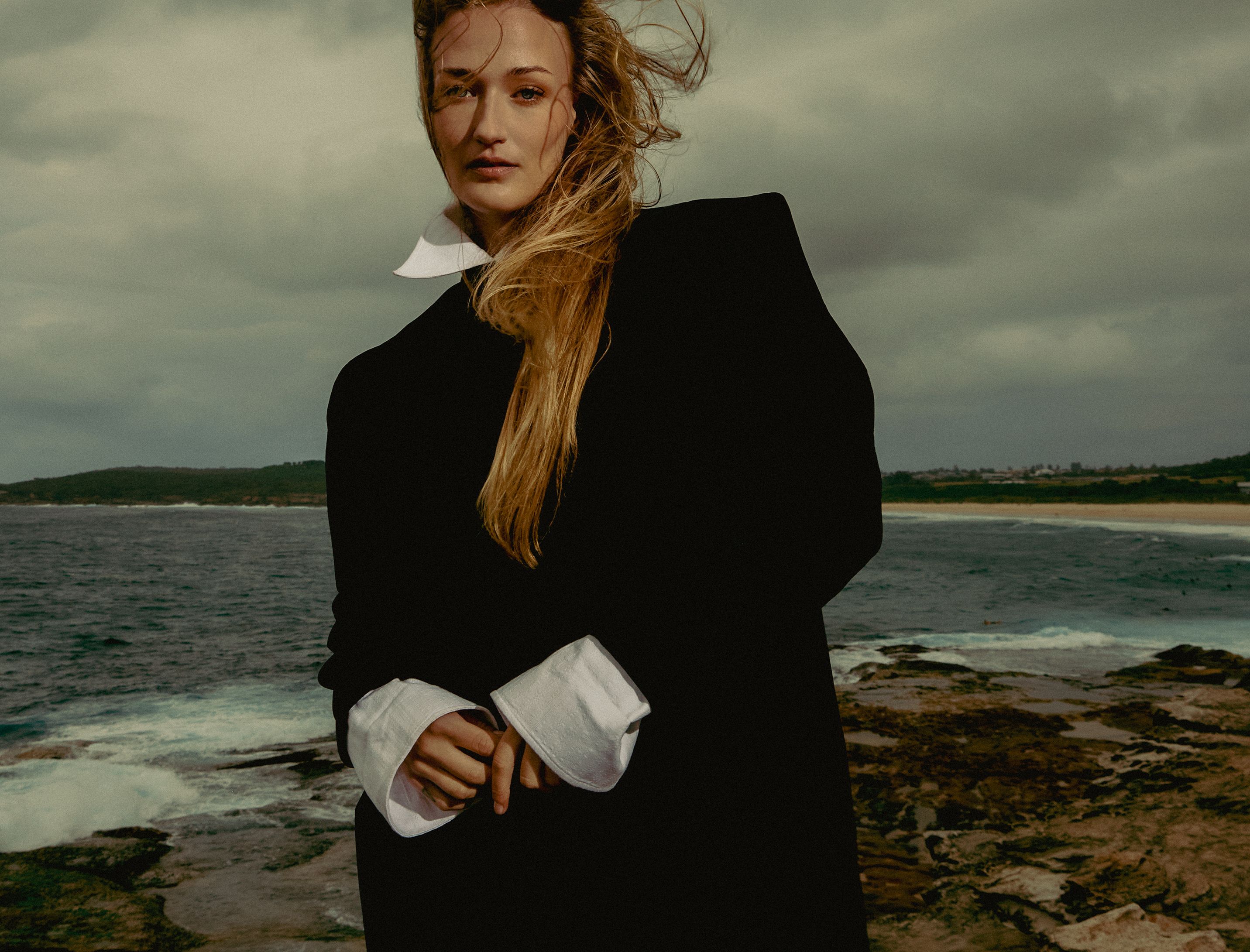 Editorial fashion photography featuring a model in architectural, minimalist clothing standing against a stark concrete backdrop.