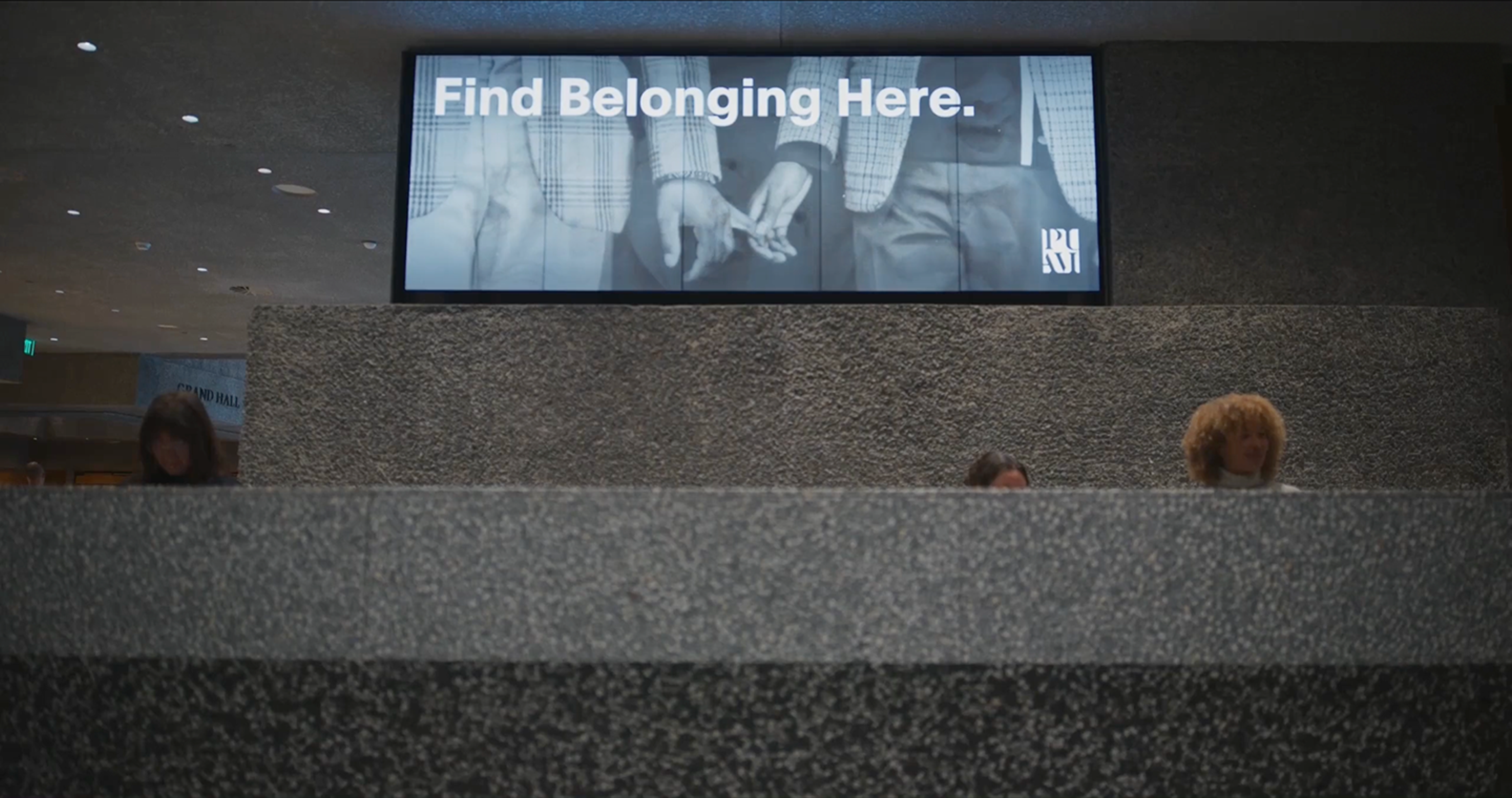 Children skip through a lobby filled with adults while behind them a large digital screen shows exhibition information for Toshiko Takaezu and an image of a large fire-glazed ceramic vessel