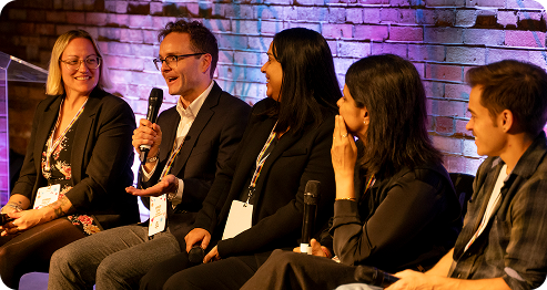 A group of people seated on a stage engaged in a discussion, with microphones in front of them.