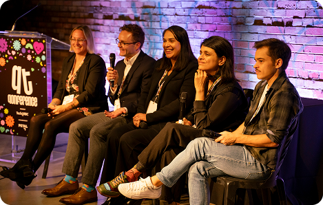 A group of people seated on chairs in front of a textured brick wall, engaged in conversation.