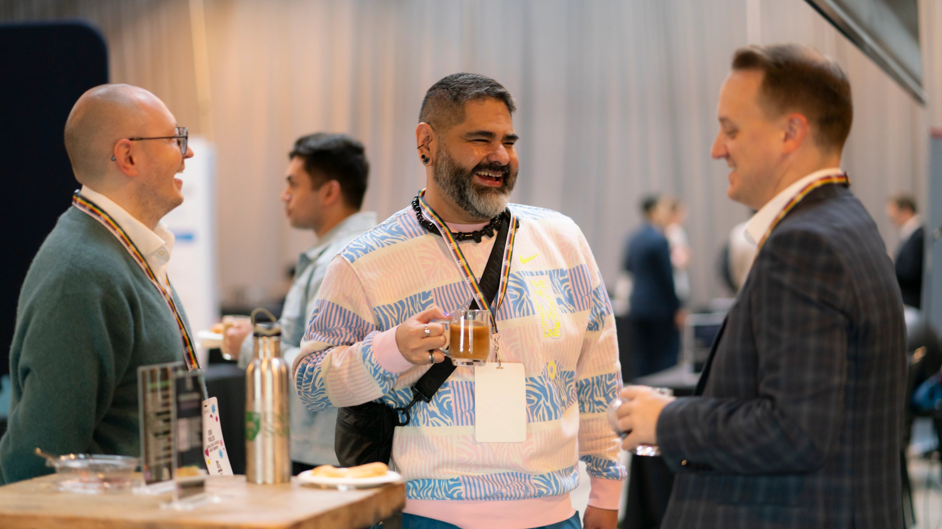 Three people are engaged in lively conversation at a networking event. They smile warmly, holding drinks, conveying a friendly and collaborative atmosphere.