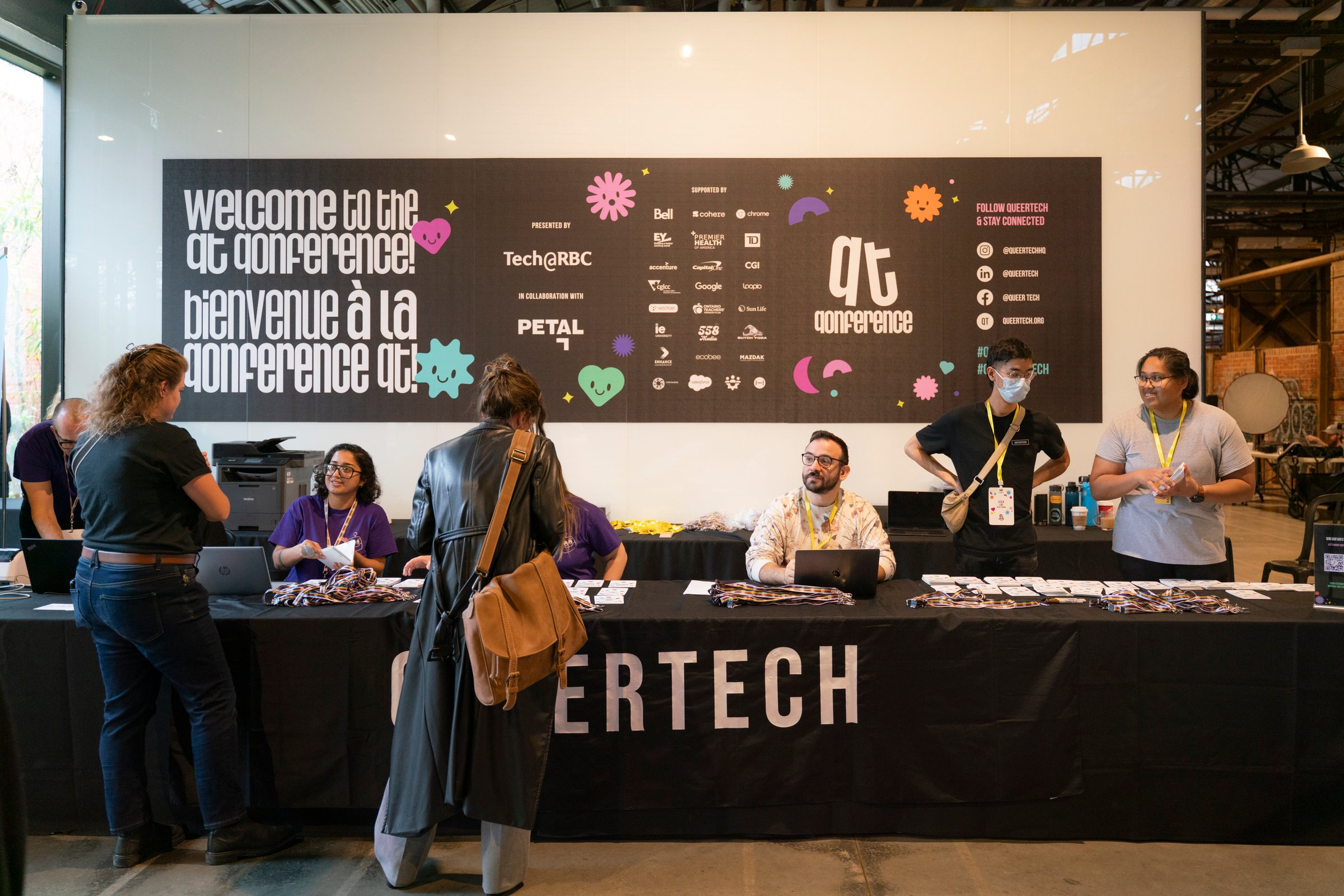 multiple people arriving at a table with the word QueerTech picking up their conference badges.