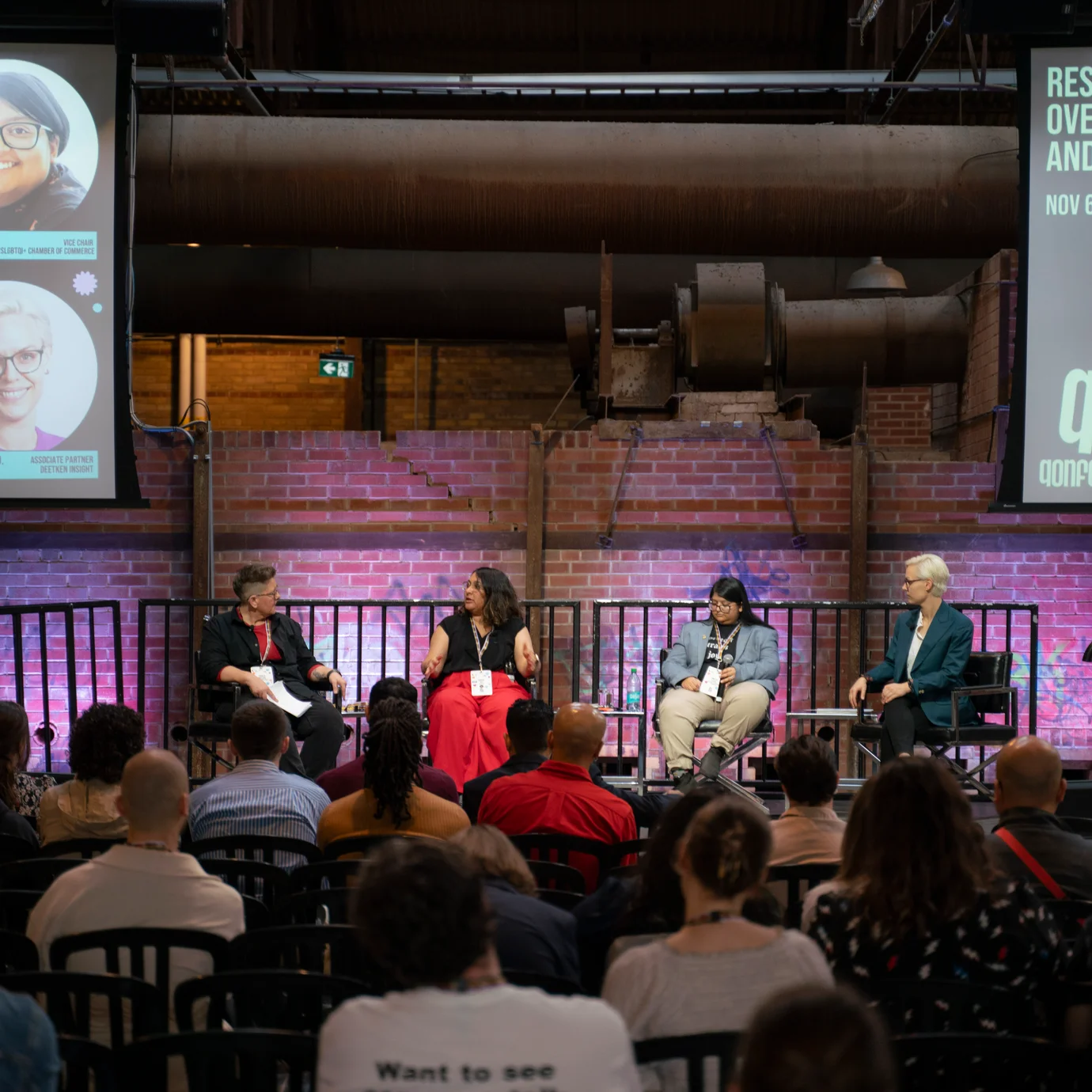 Panel discussion on stage at QTQ with speakers seated and audience watching, large screens displaying session details.