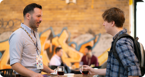 Two men engaged in conversation at a table, each holding a drink, sharing a moment of camaraderie.