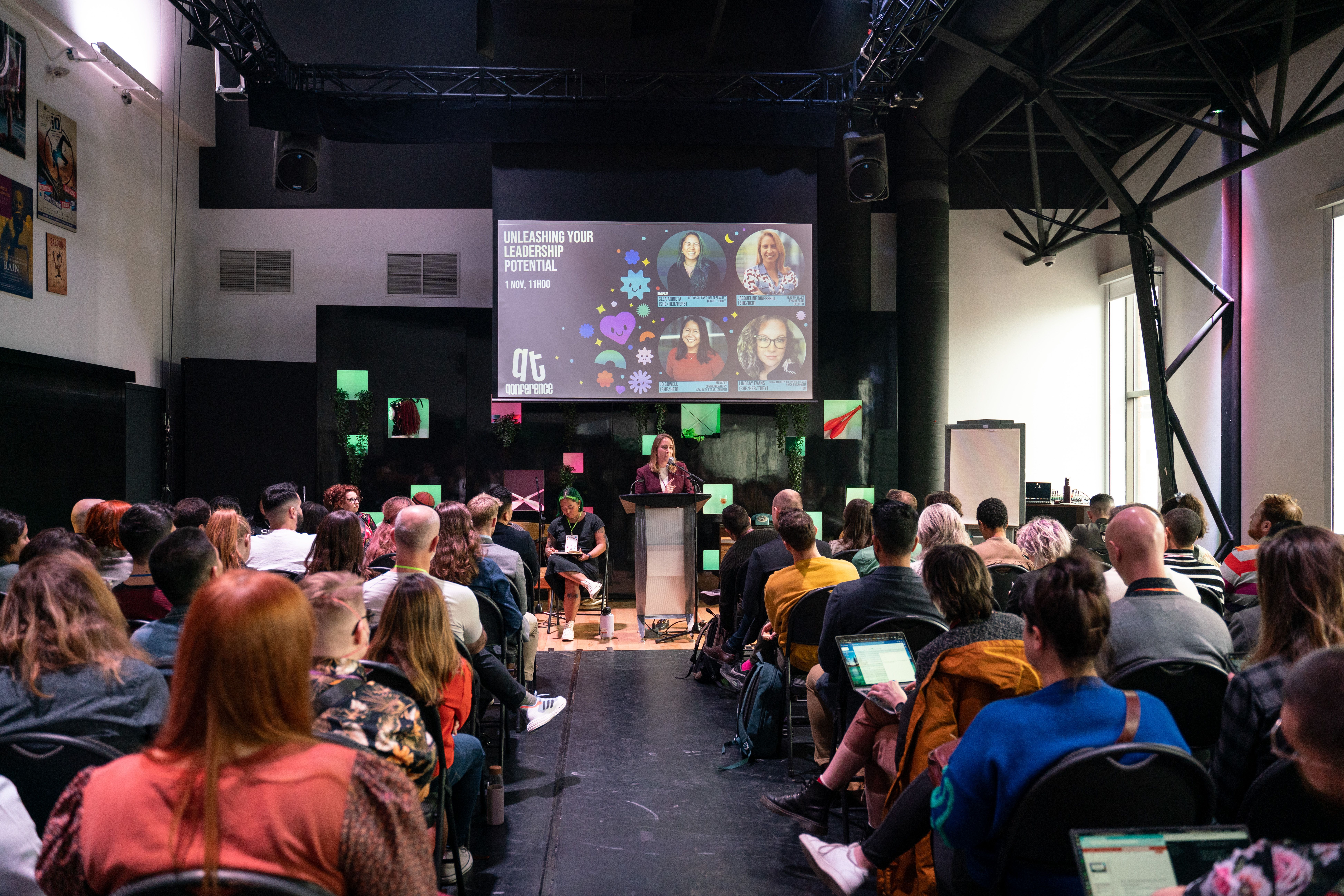 A speaker presents to a seated audience in a modern conference room. A large screen displays "Unleashing Your Leadership Potential" with speaker images.