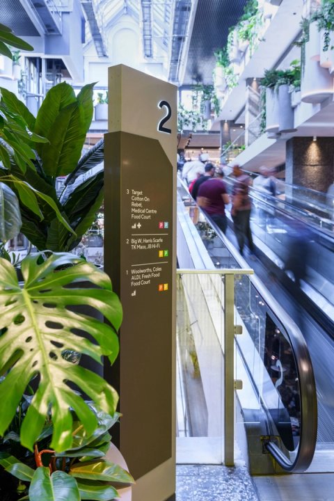 Level directory sign infront of escalator and green plants