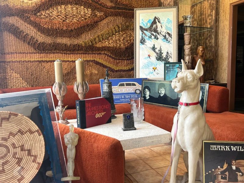 Toluca Lake Hollywood insider estate sale room display with orange sofa, woven tapestry, Beatles photograph, James Bond book, art, and white dog statue.