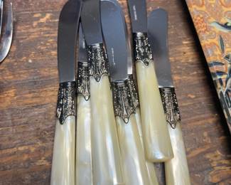Set of vintage knives with pearl-style handles and ornate metal collars, displayed on a wood table at a Beverly Hills estate sale.