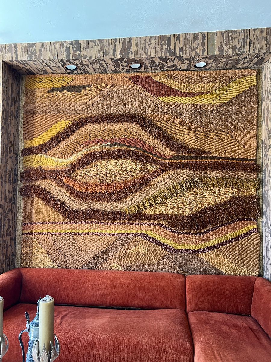 Large woven wall tapestry displayed above an orange mid-century sofa in a Toluca Lake Hollywood insider estate.