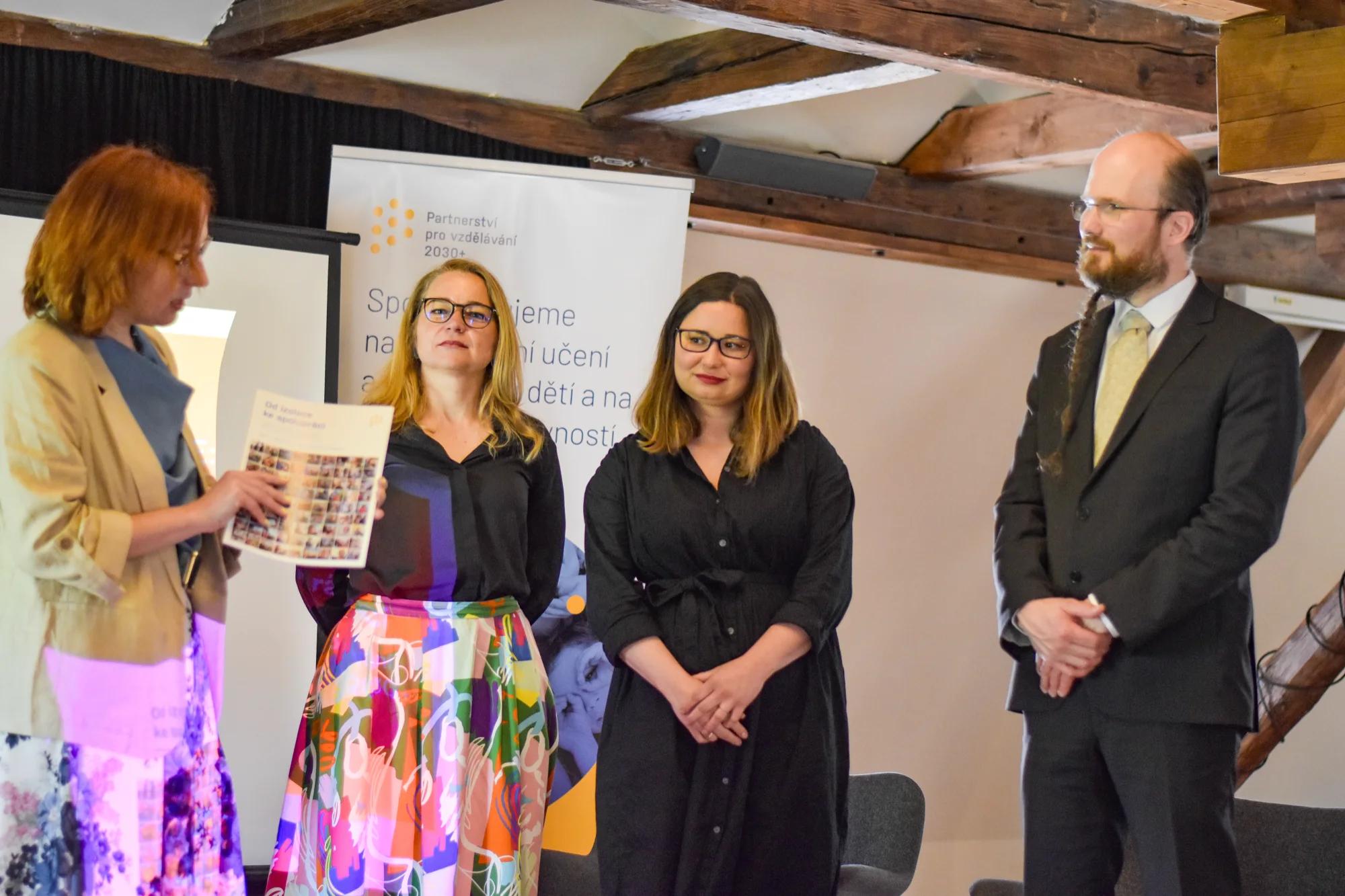 Čtyři lidé u rollupu Partnerství pro vzdělávání 2030+ během setkání