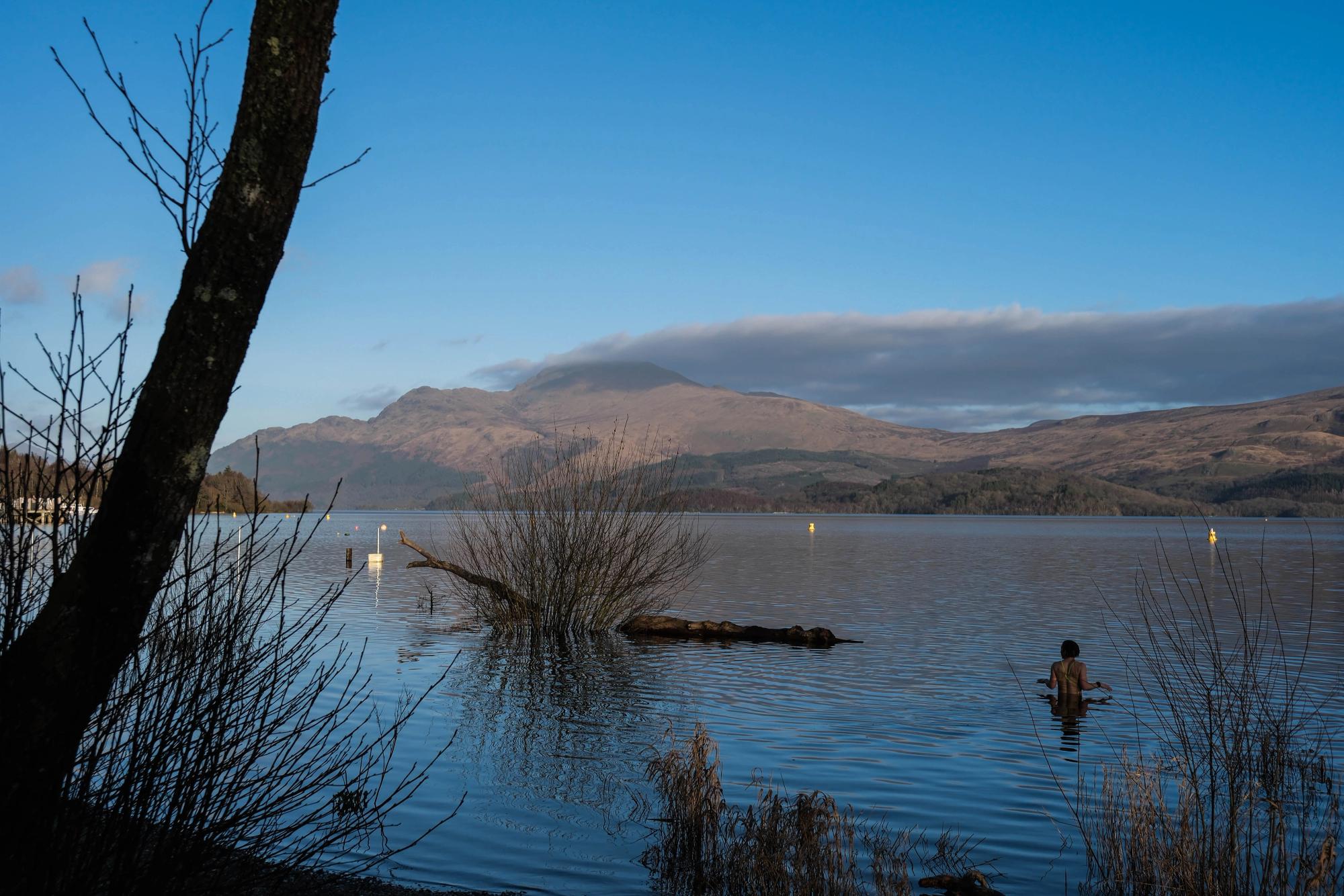 A woman walking in the loch with clear skies and Ben Lomond in the background