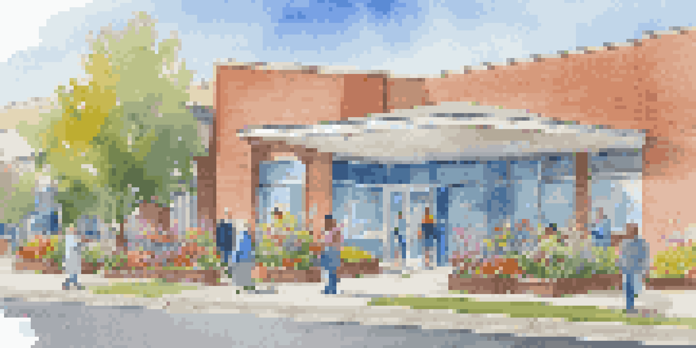 A modern community health clinic with large windows, busy healthcare professionals, and diverse patients, surrounded by flowers and a clear blue sky.