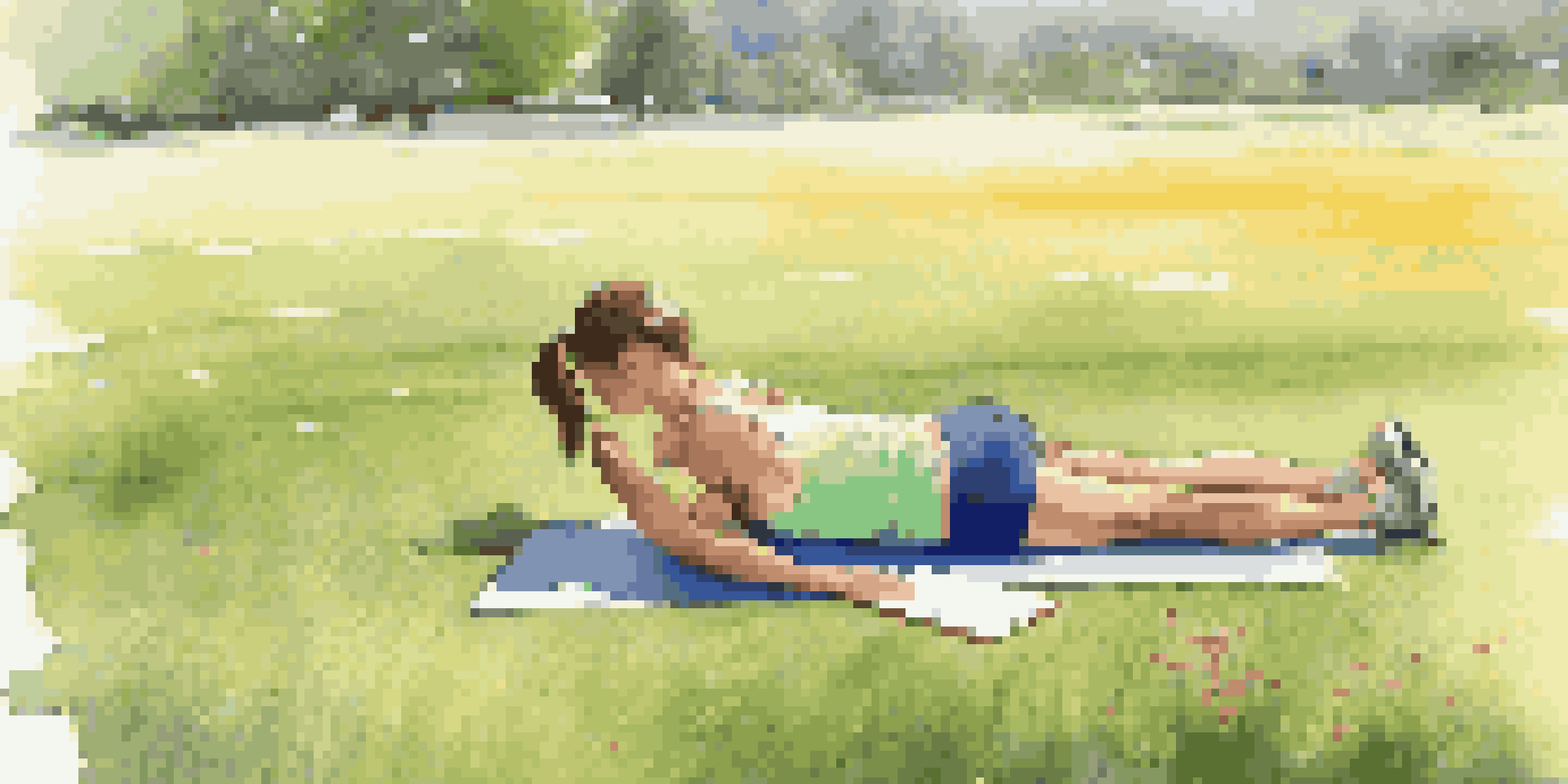 A young woman performing a flexibility test outdoors in the morning sun, surrounded by green grass and wildflowers, with a clipboard nearby.