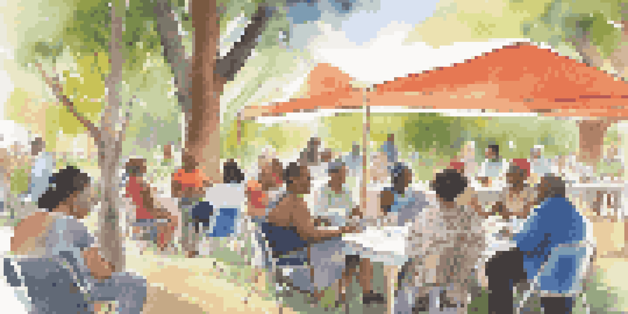 A community health workshop with diverse participants discussing health education outdoors under soft sunlight.