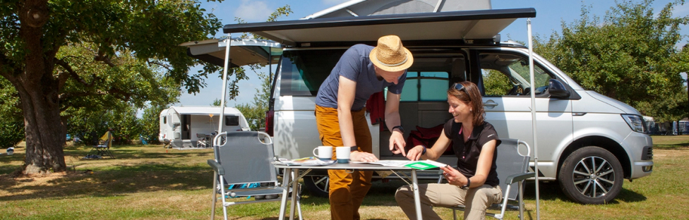 Koppel kijkt op kaartje aan tafel met camper op de achtergrond