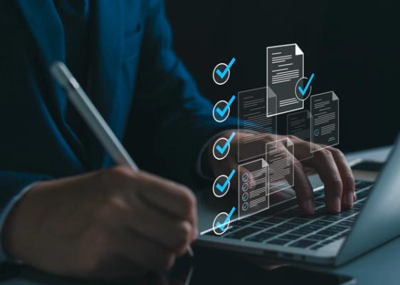 Laptop met man erachter en documenten met vinkjes erbij
