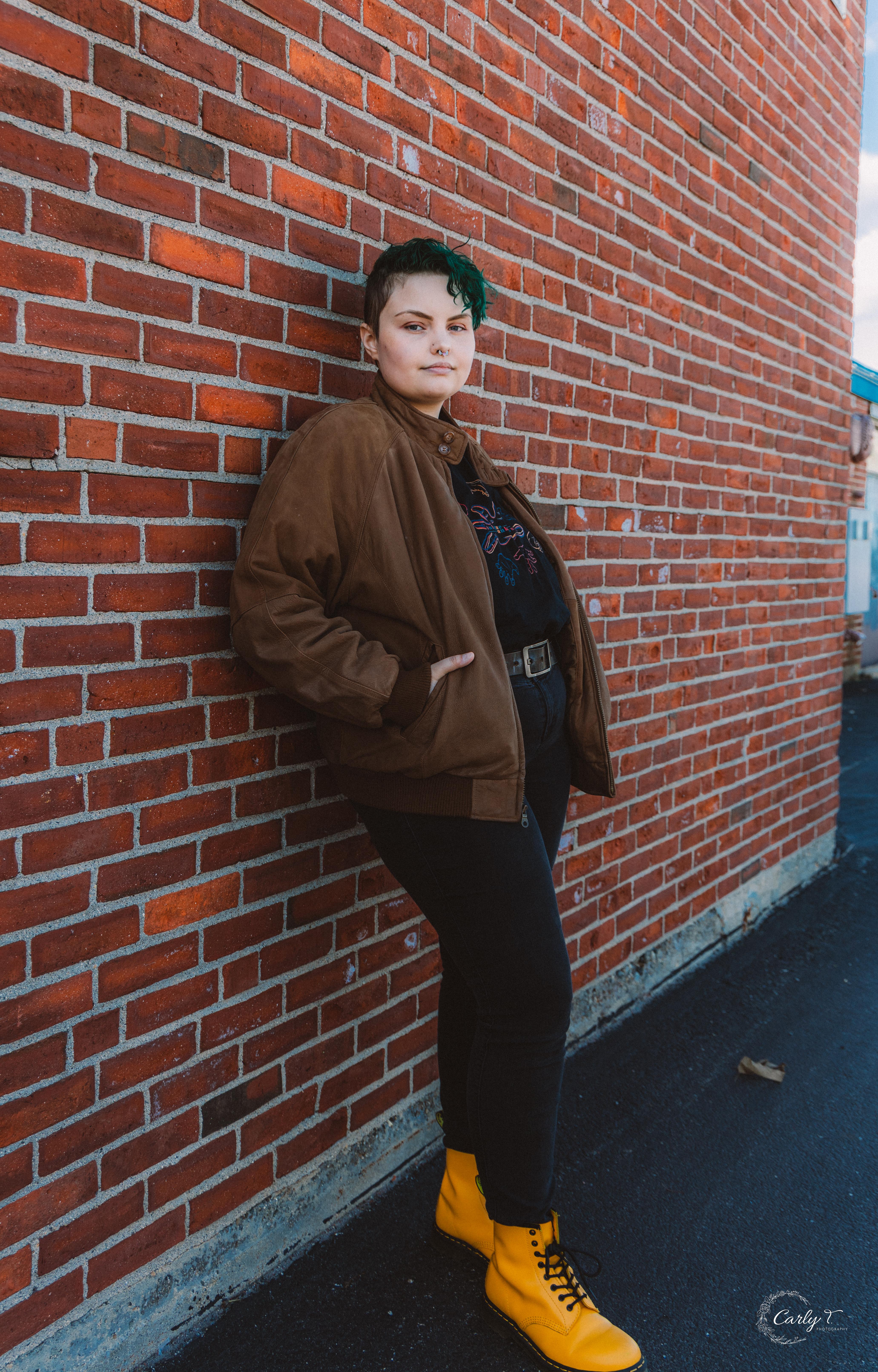 Kyah leaning against a brickwall. Photo credit WCKD collective.