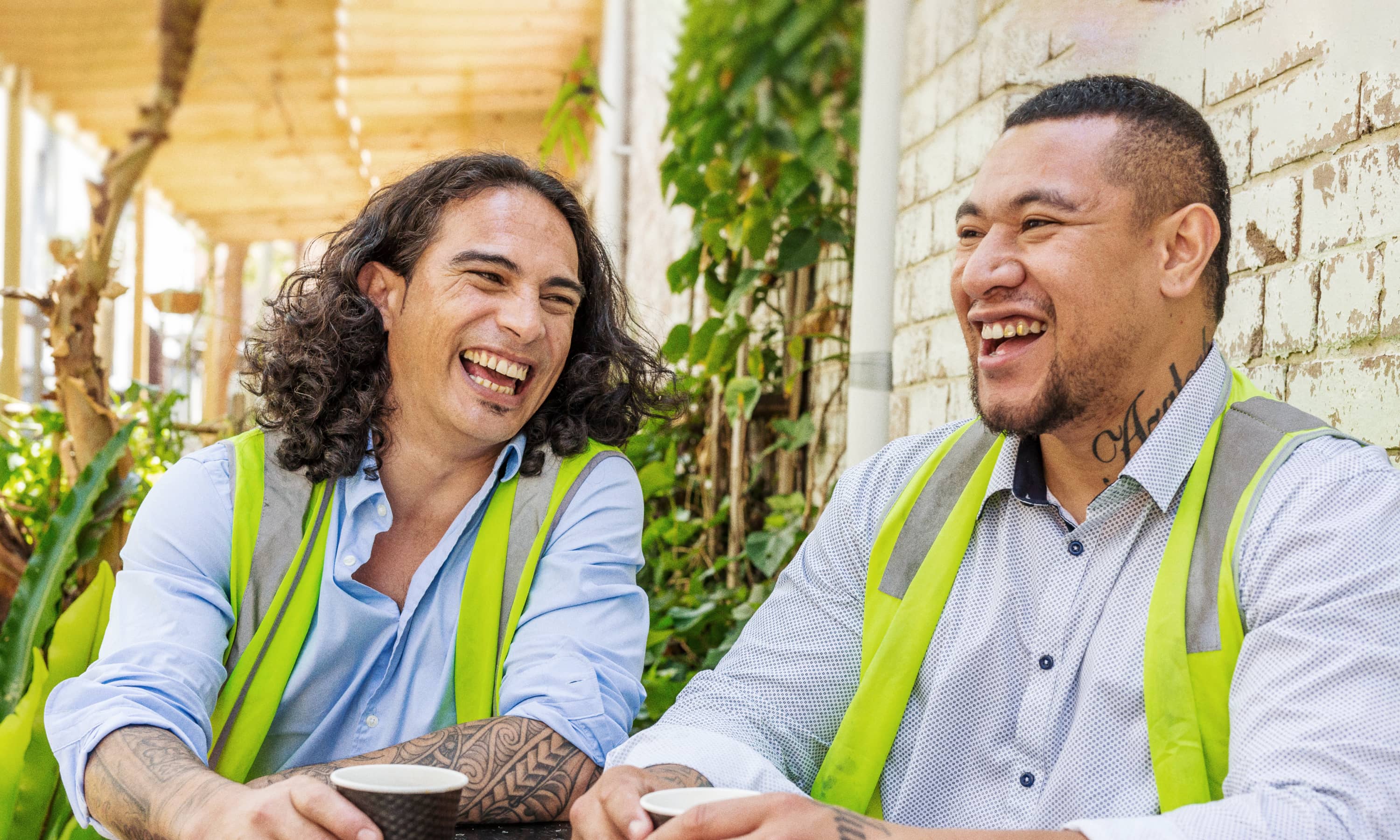 Two men in hi-vis vests laughing and talking about their gambling experiences 