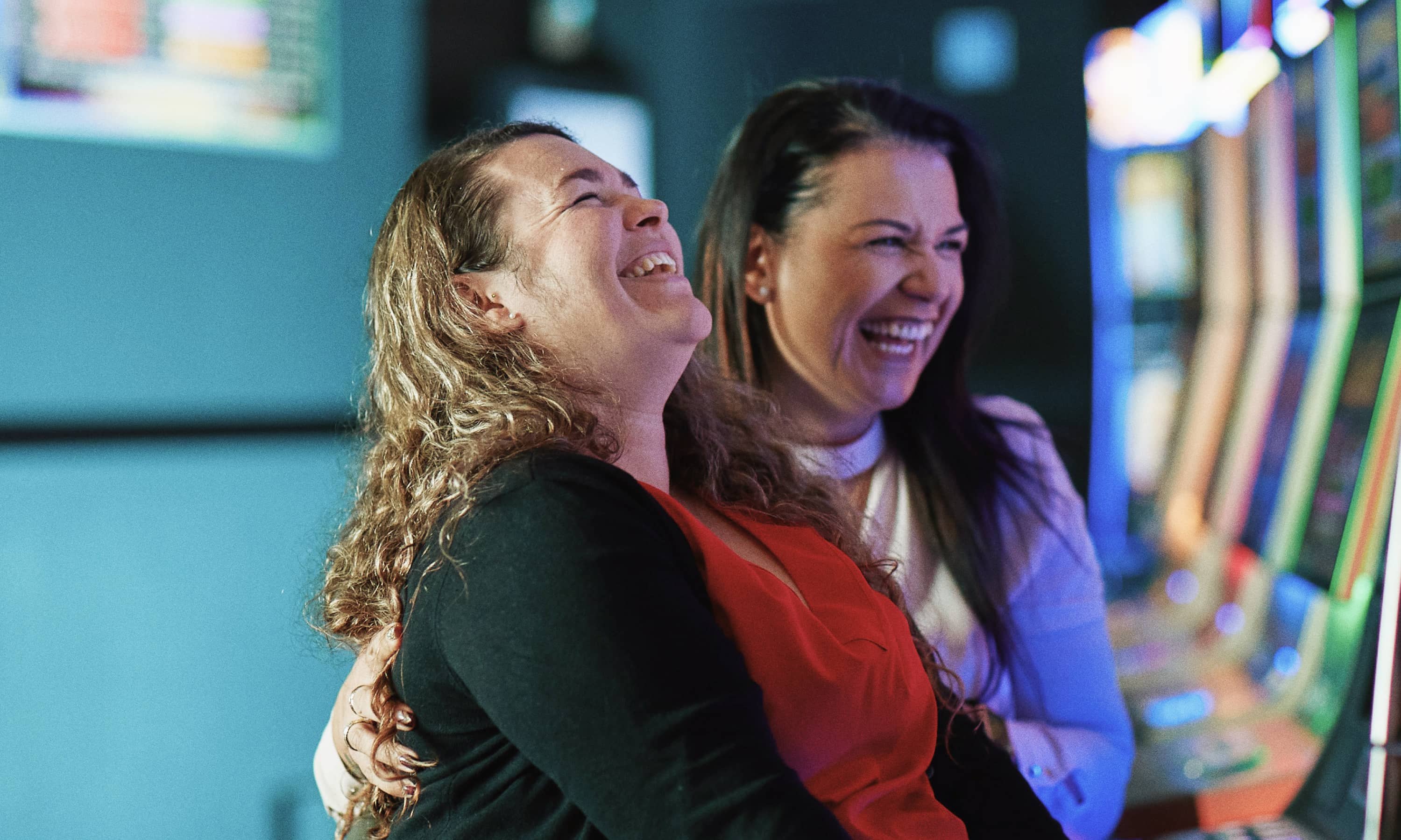 Two women using a pokie machine and laughing together