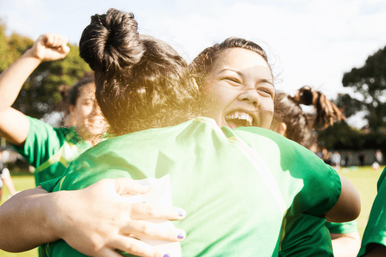 A group of girls on a sportsfield hugging and cheering 