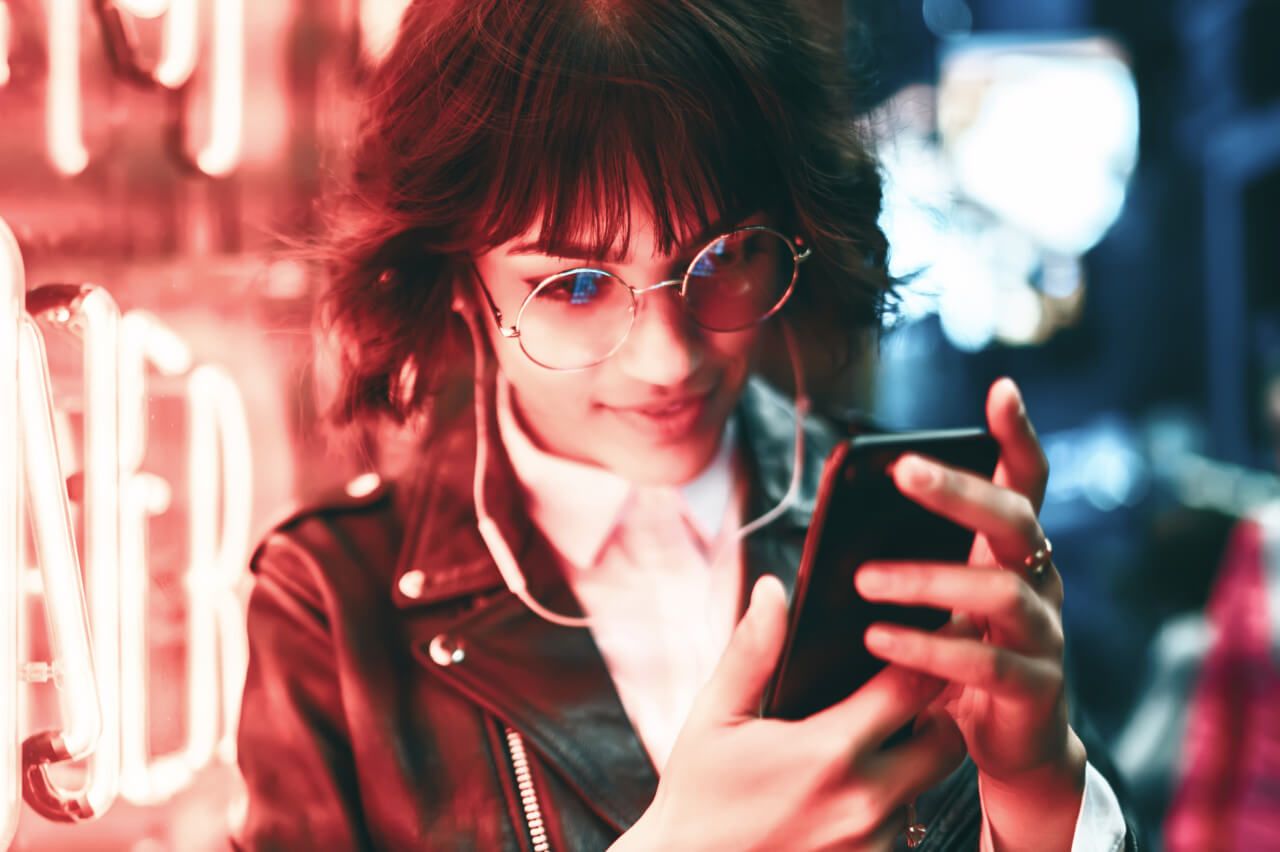 Girl outside a store with bright lights looking at phone 