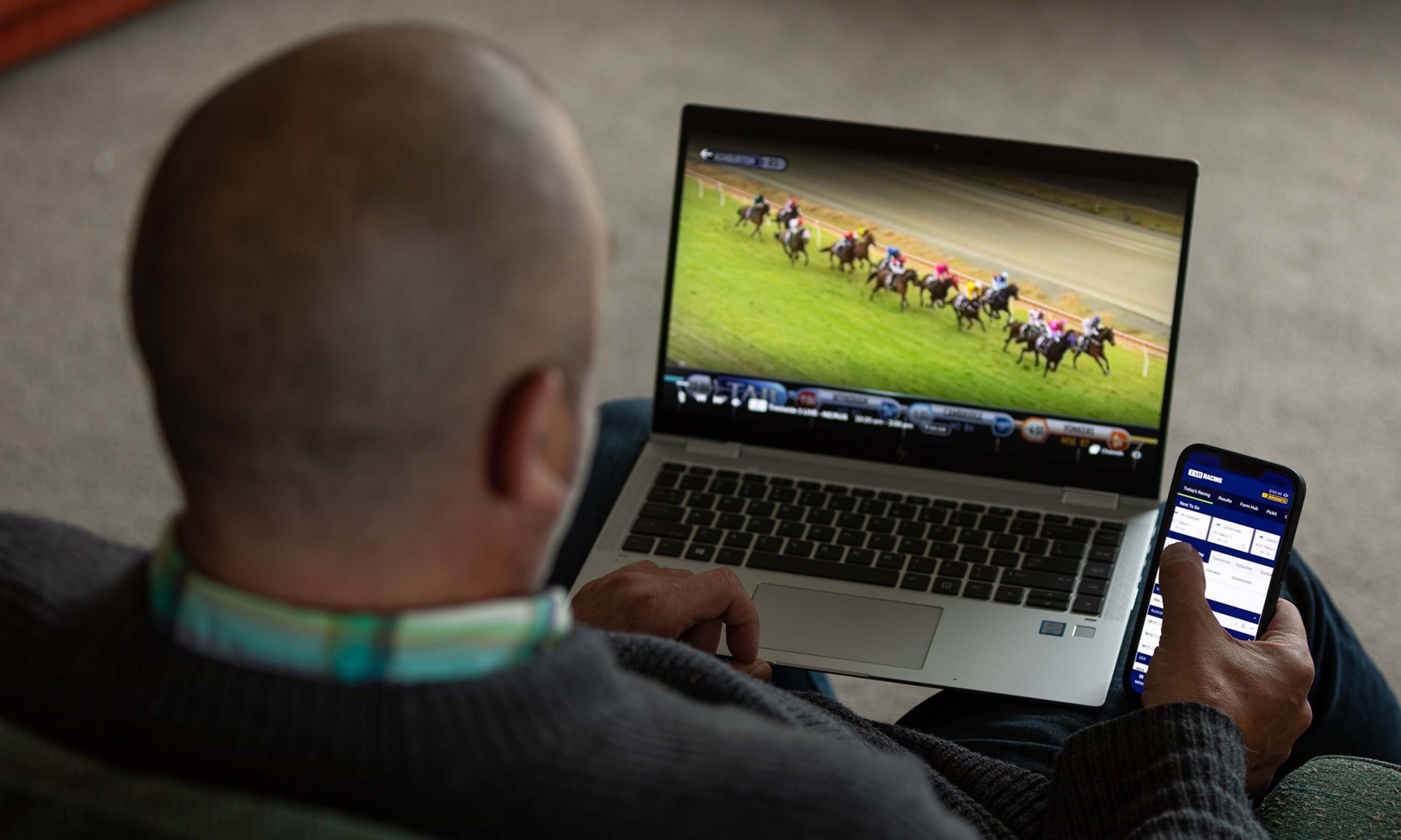 Man watching horse races on laptop while placing bets on phone