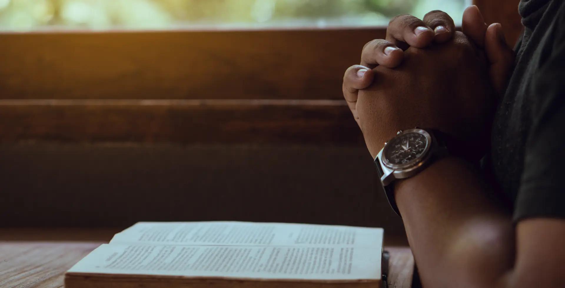 Hands joined in prayer over an open Bible