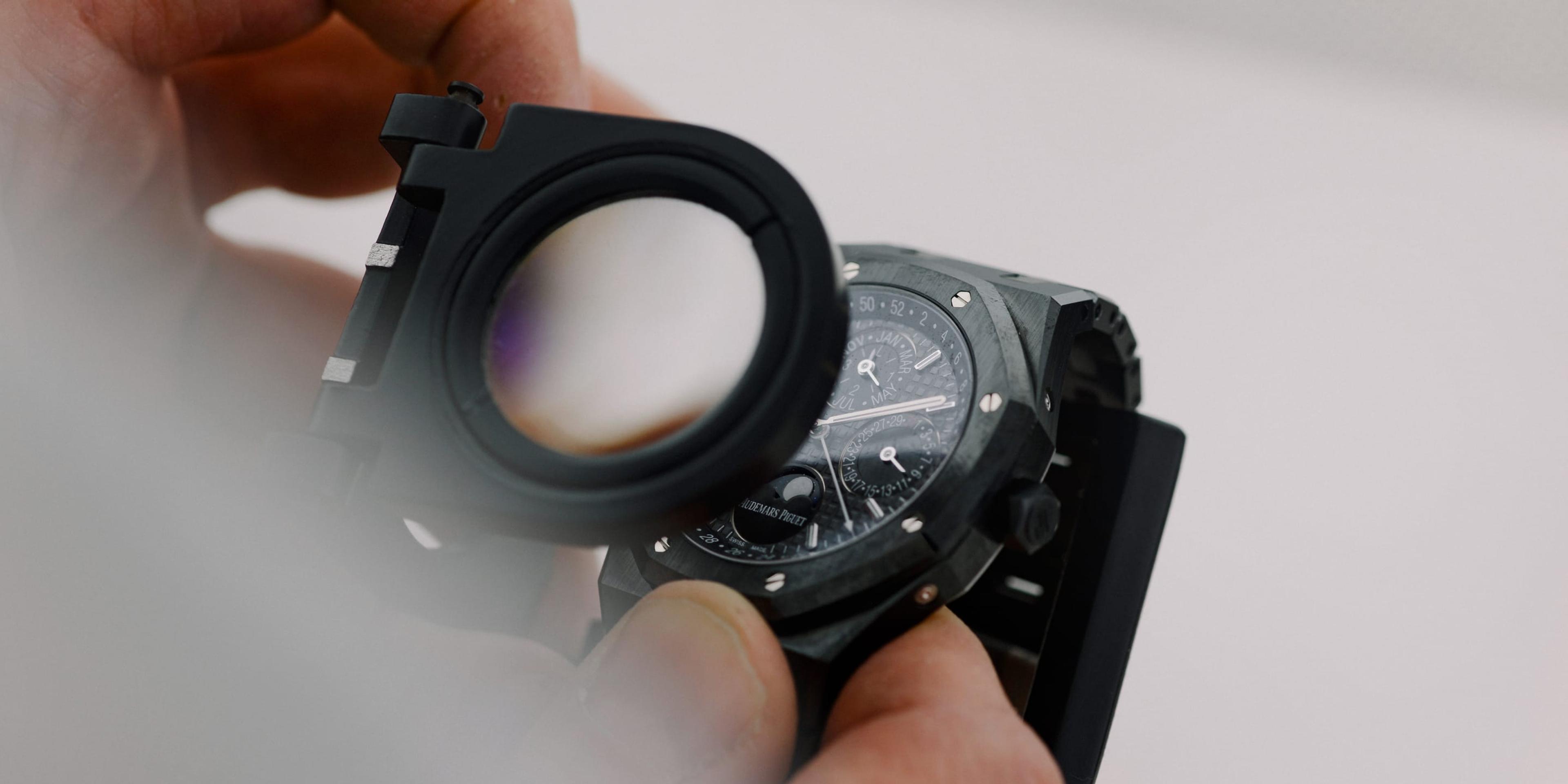 Someone views a watch face using a loupe