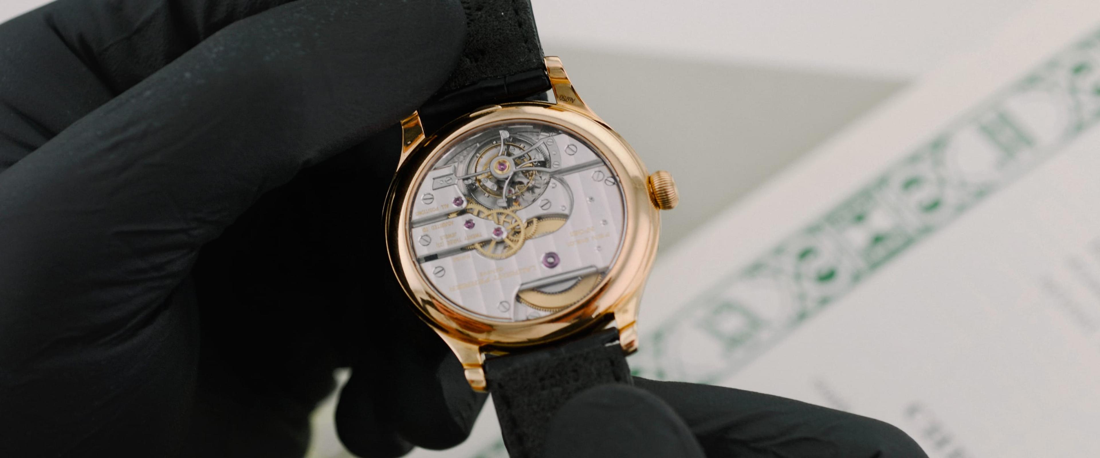 A watch being handled with black gloves