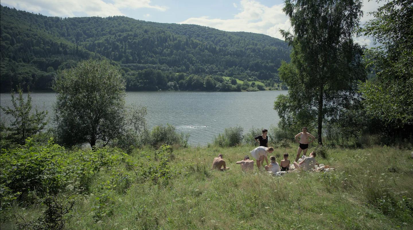 a group of people sitting on a hill by a lake
