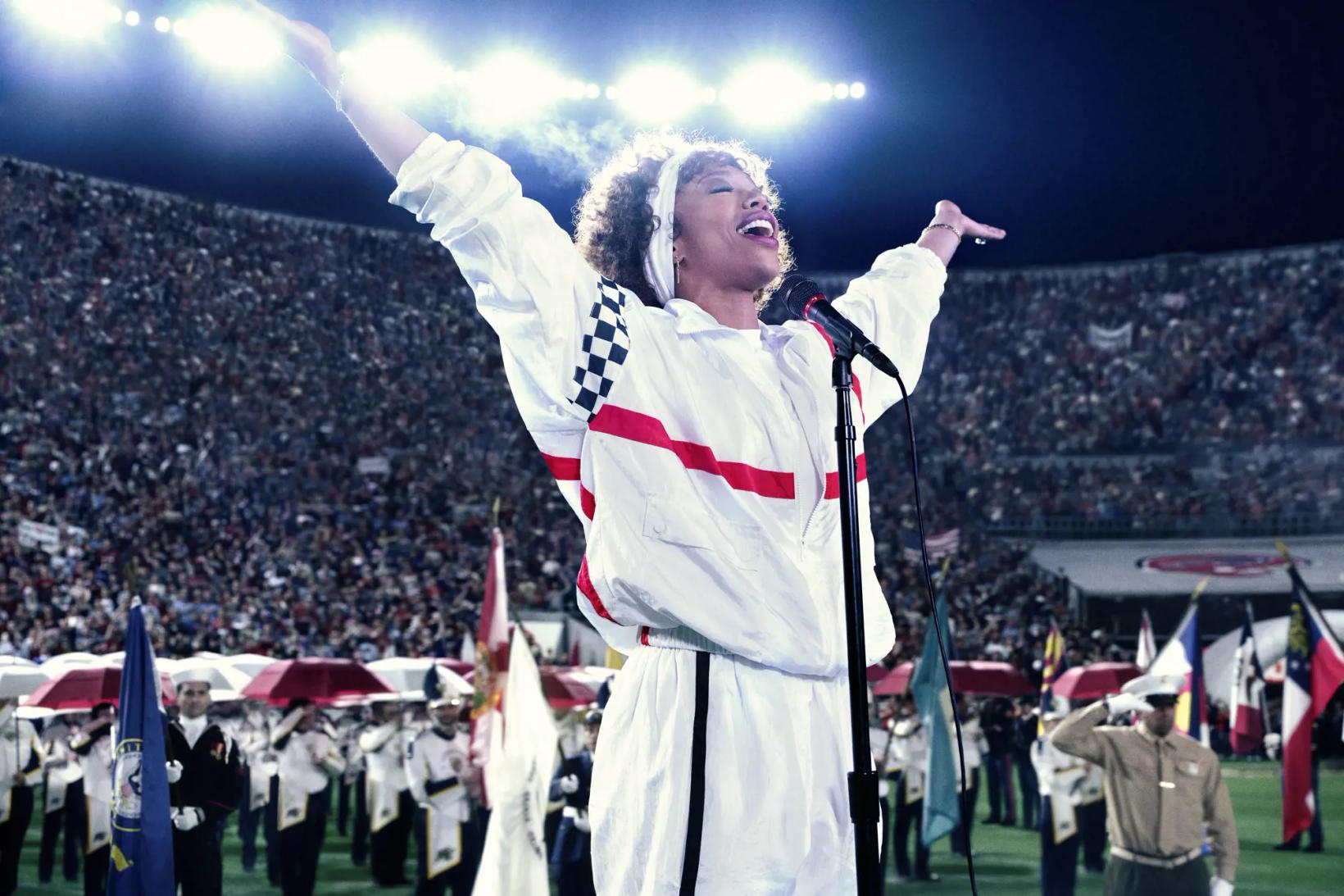 a man in a white robe and red scarf with a microphone in front of a crowd of people
