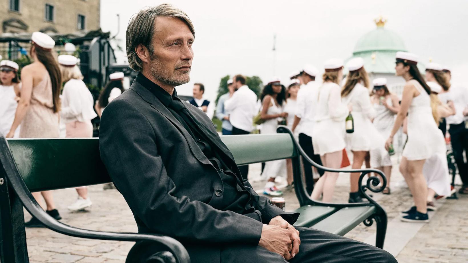Mads Mikkelsen sitting on a bench