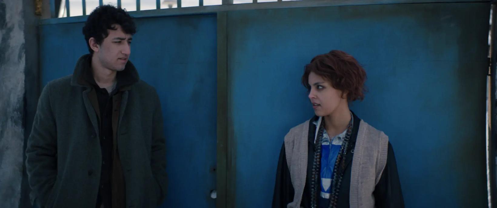 a man and a woman standing next to a blue wall