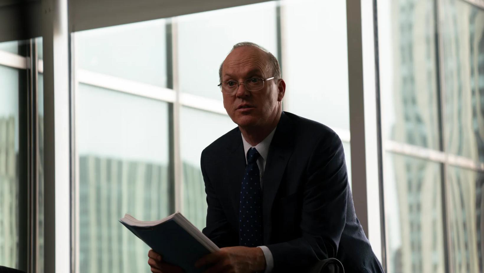 Michael Keaton in a suit holding a book
