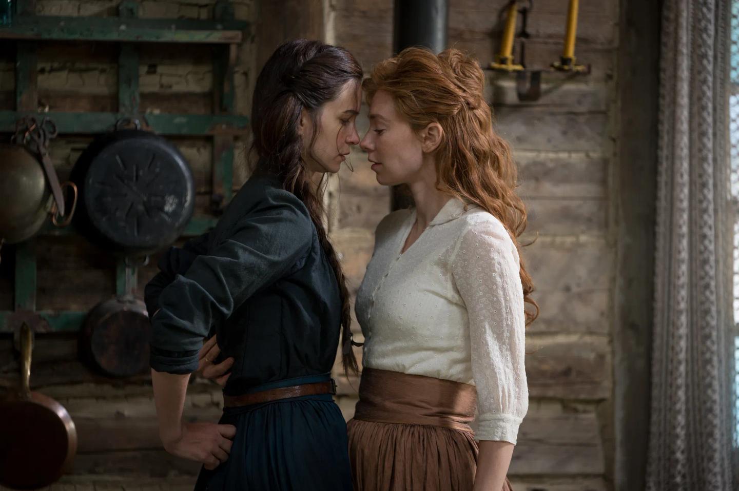 two women kissing in front of a wooden building