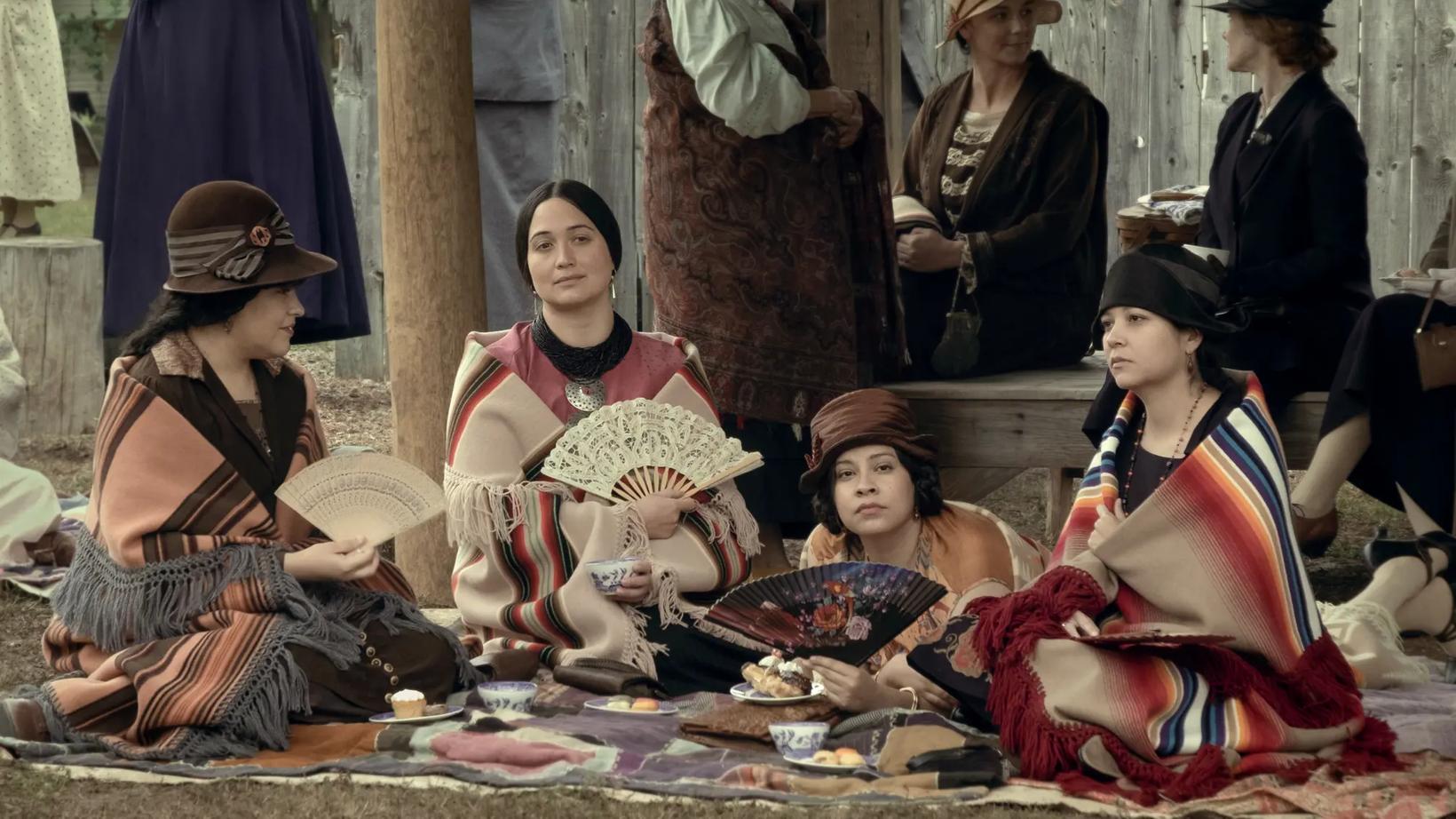 Lily Gladstone et al. sitting on the ground with hats on