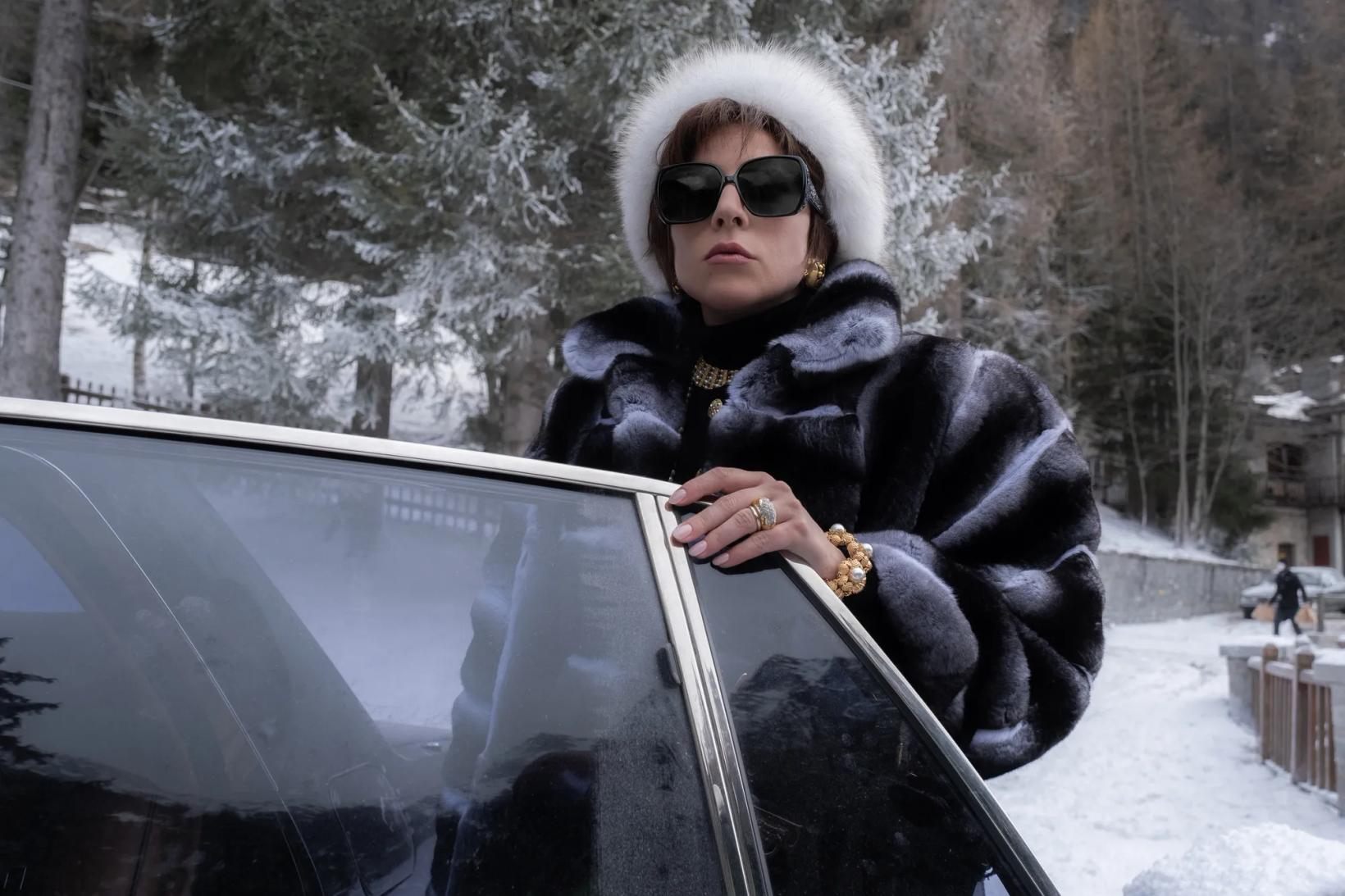 a person in a fur coat and sunglasses sitting on a car