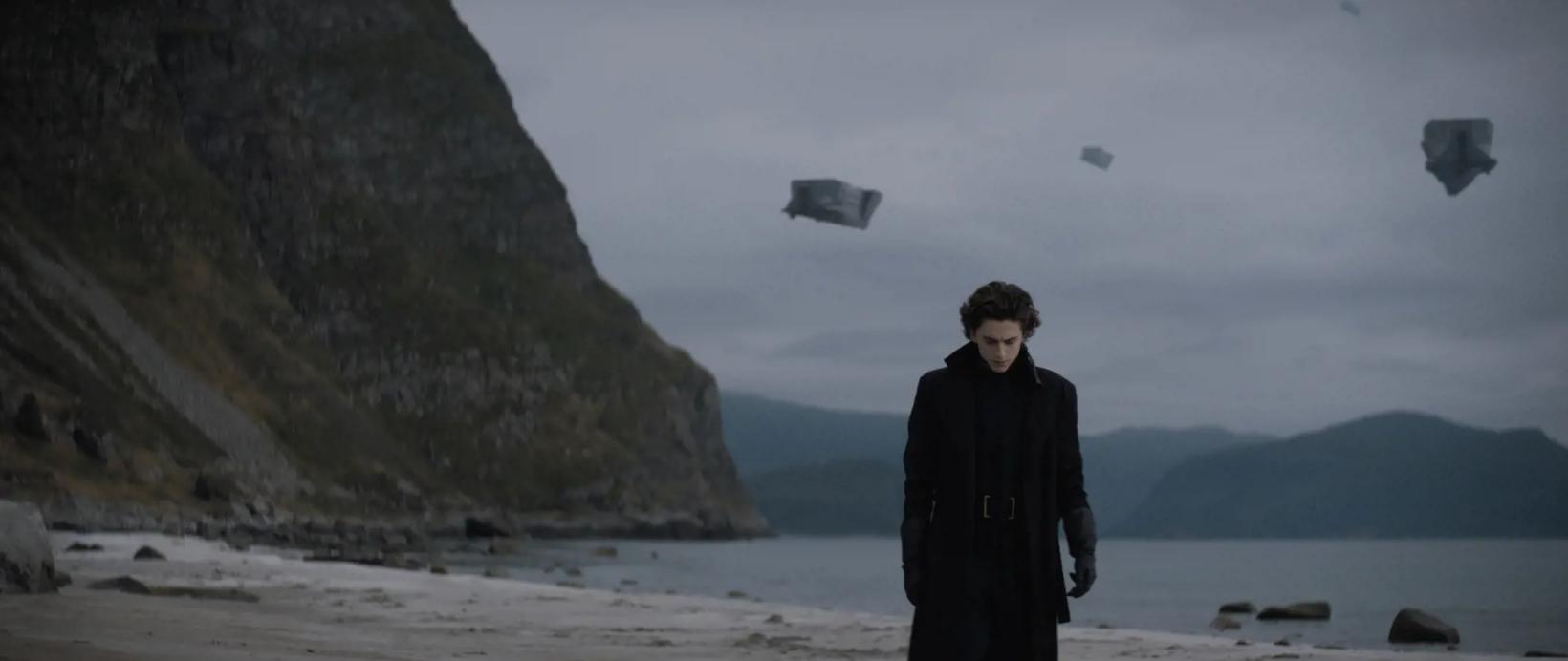 a man standing on a beach with a kite flying in the sky