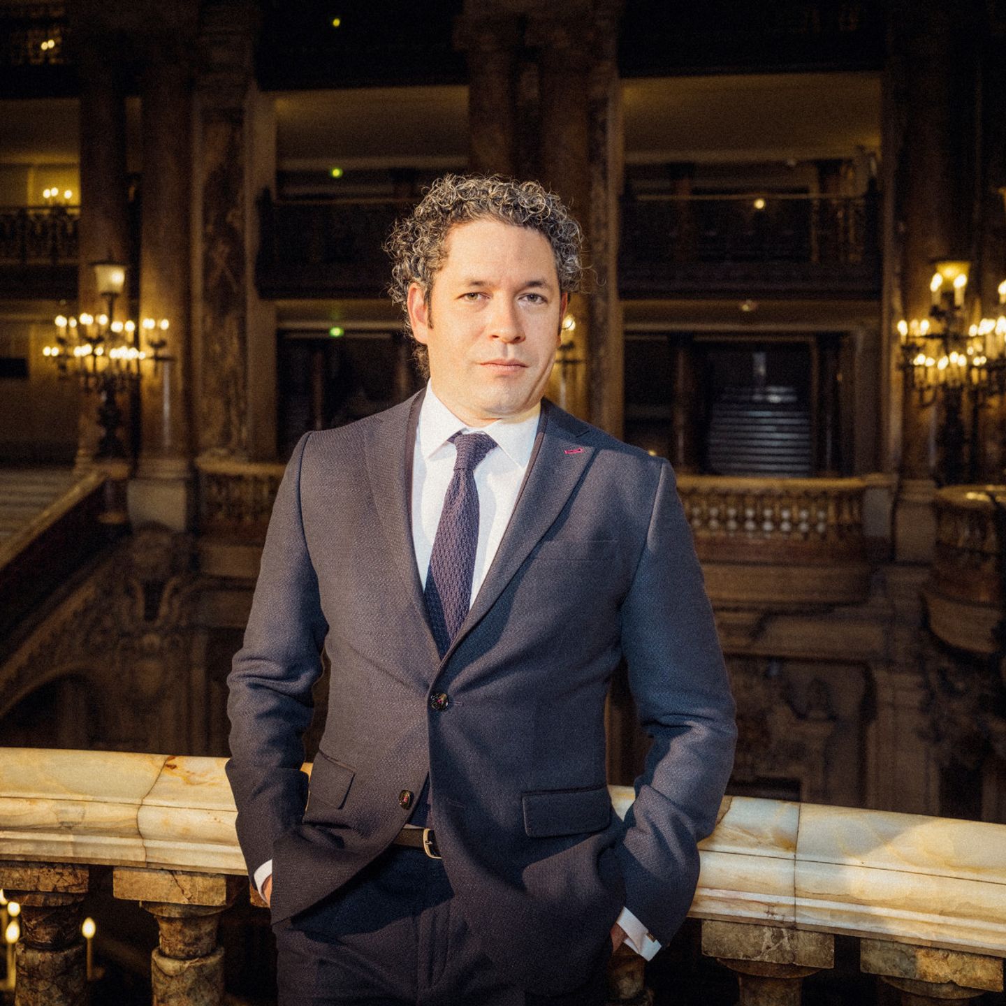 Gustavo Dudamel in a suit sitting on a bench