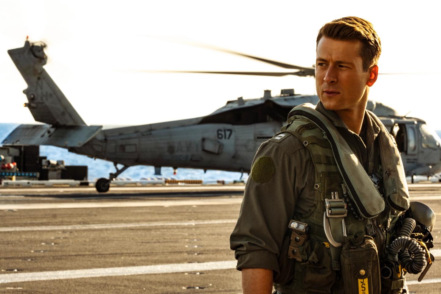 Glen Powell in uniform standing in front of a helicopter