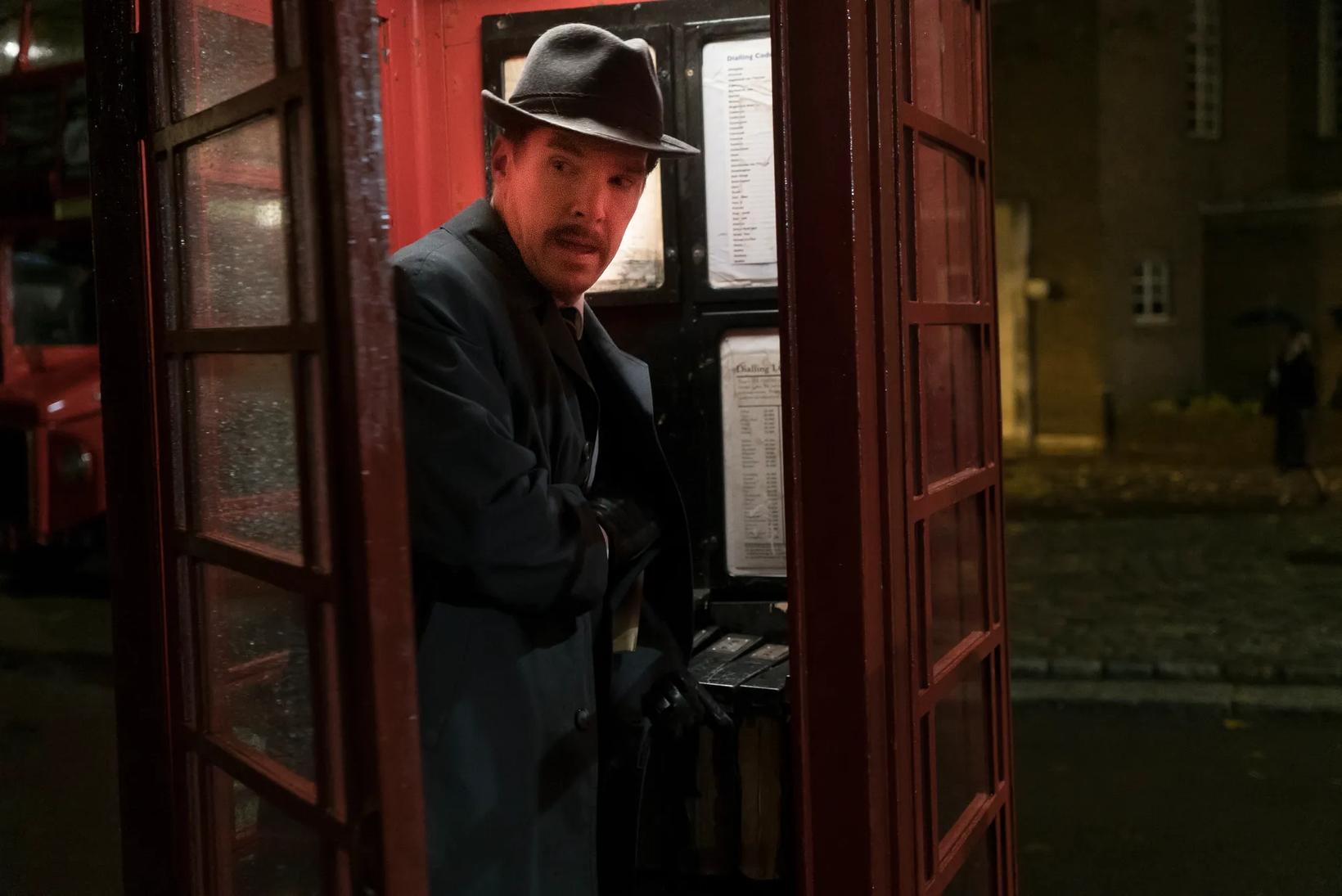 Benedict Cumberbatch in a suit and hat leaning against a telephone booth