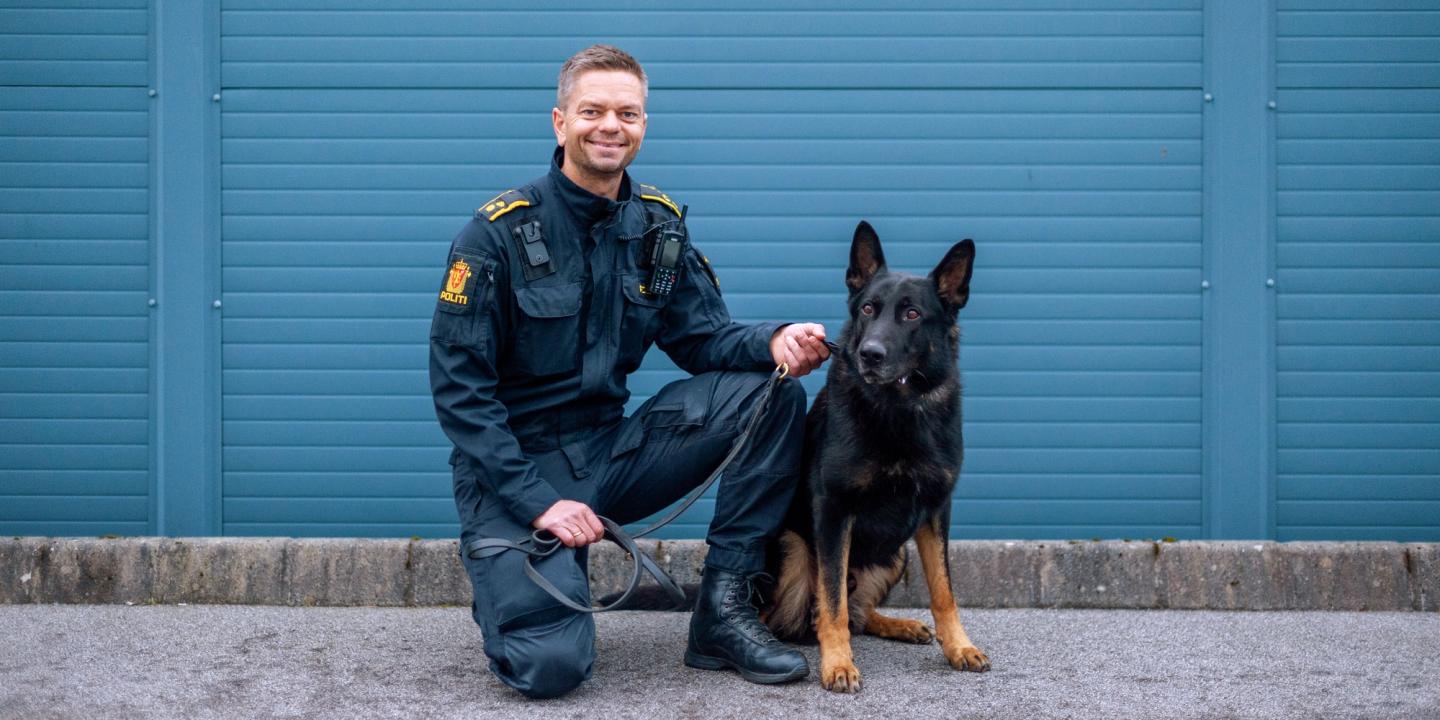 En norsk politimann smiler til kamera, ved siden av en schæfer, i et promobilde for serien Politihundene.