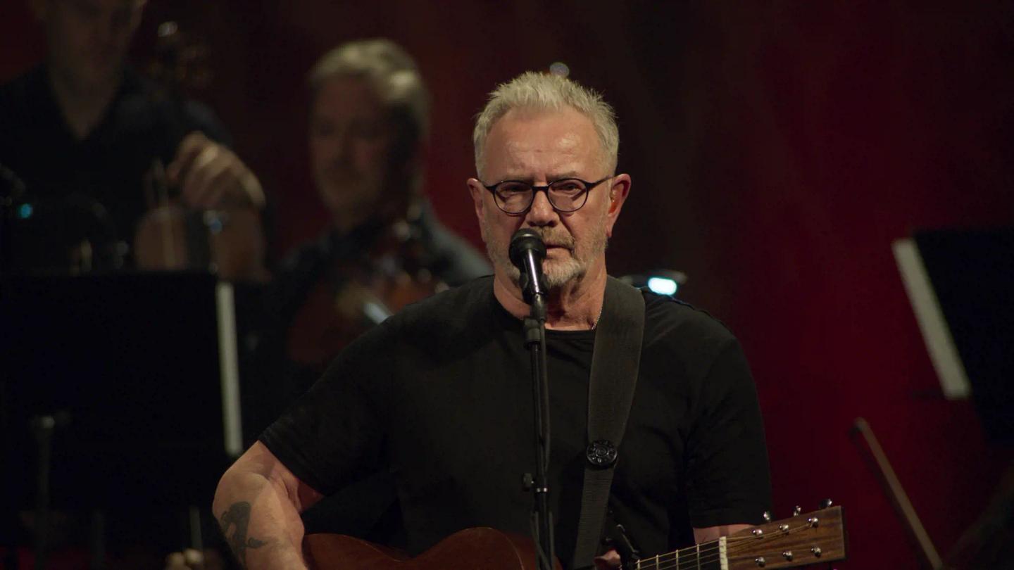 Åge Aleksandersen with a beard and glasses holding a microphone