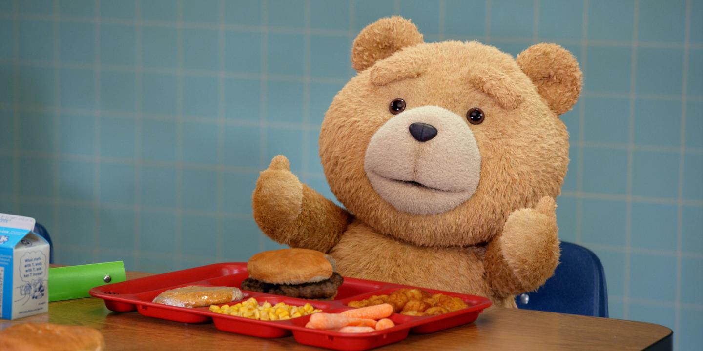 Bamsen Ted gir to tomler opp. Han sitter ved et bord med kantinemat i Ted sesong 1.