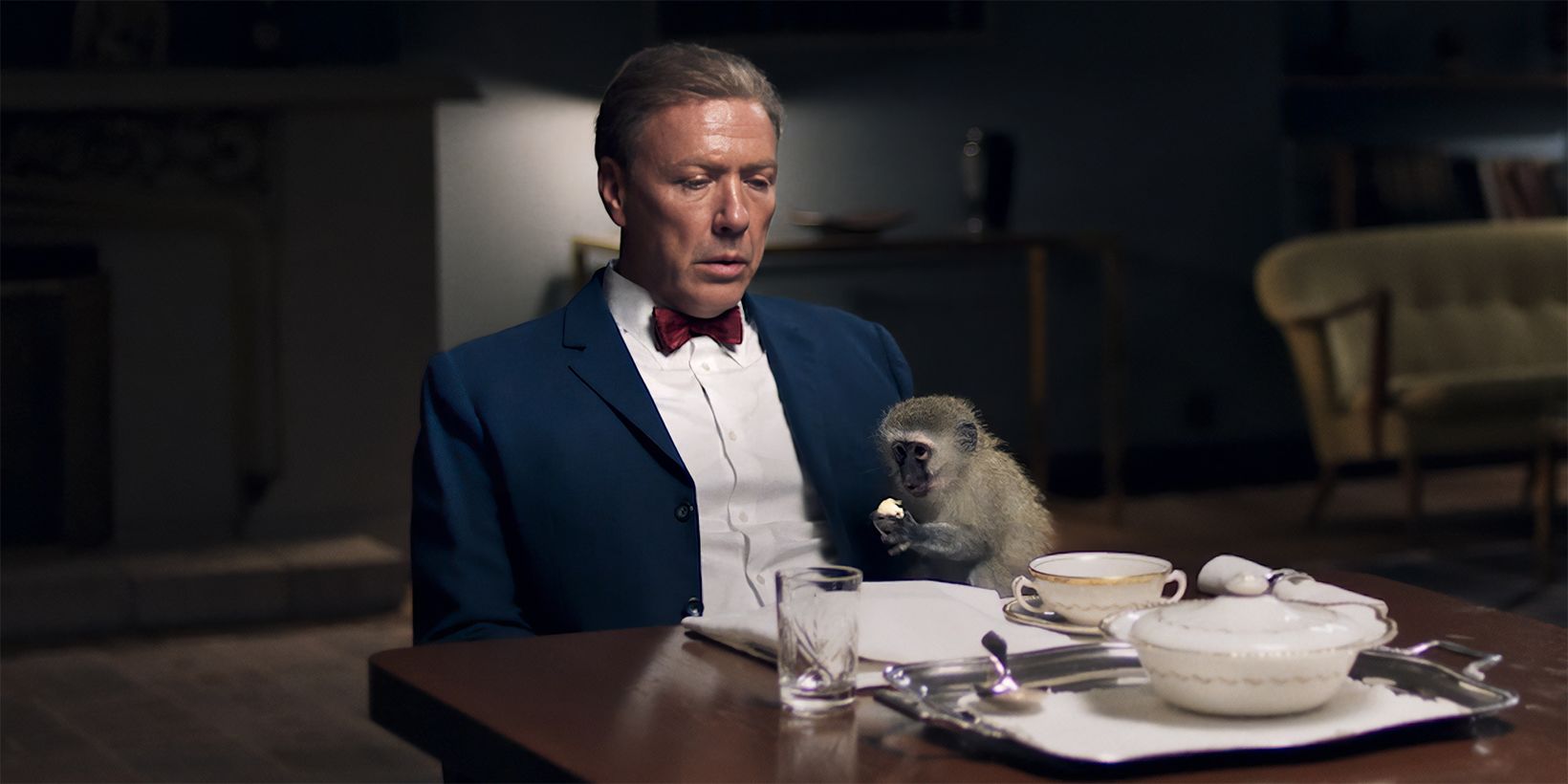 Mikael Persbrandt og en ape sitter ved middagsbordet i Hammarskjöld