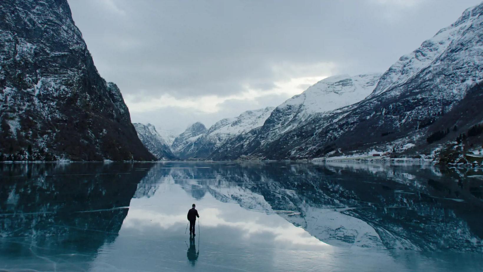 a person standing in a body of water surrounded by snow covered mountains