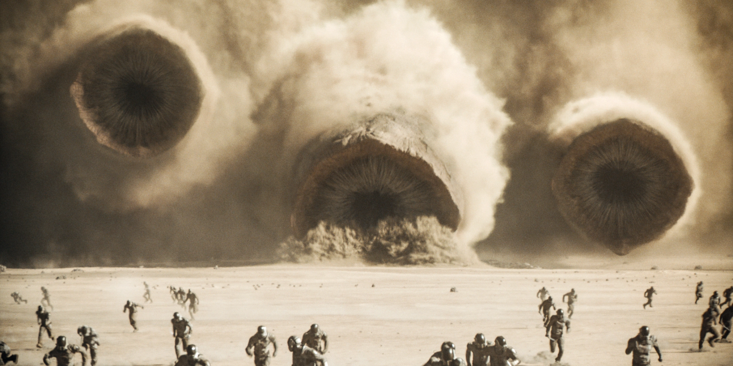 Tre sandormer i Dune: Part Two beveger seg, med munnen åpen, mot en rekke soldater som løper for livet i "Dune: Part Two".