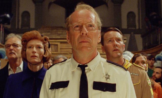 a man in a white shirt and tie with Edward Norton, Tilda Swinton et al. behind him