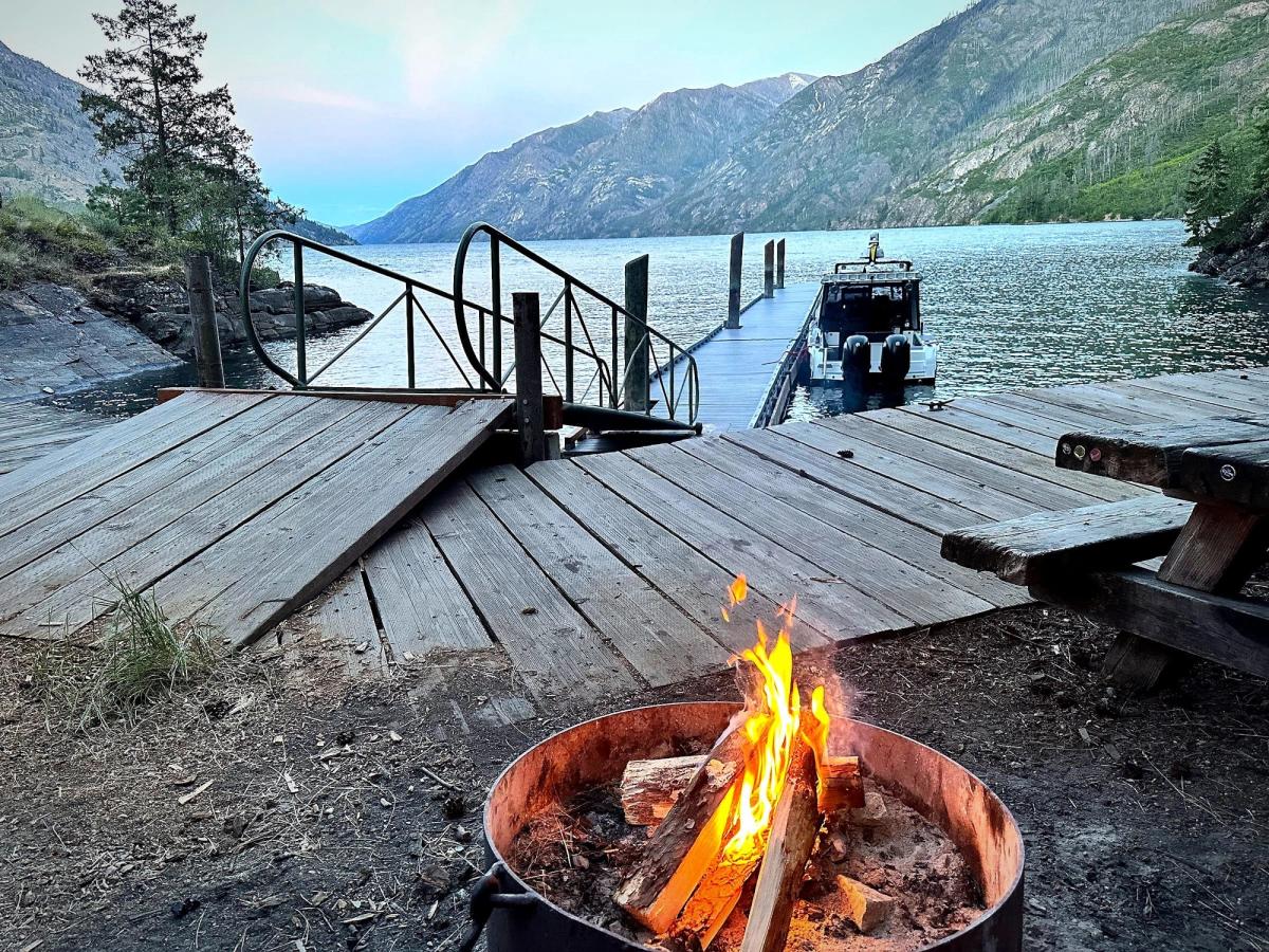 A fire ring at a lakeside campground dock at dusk, our boat moored beyond